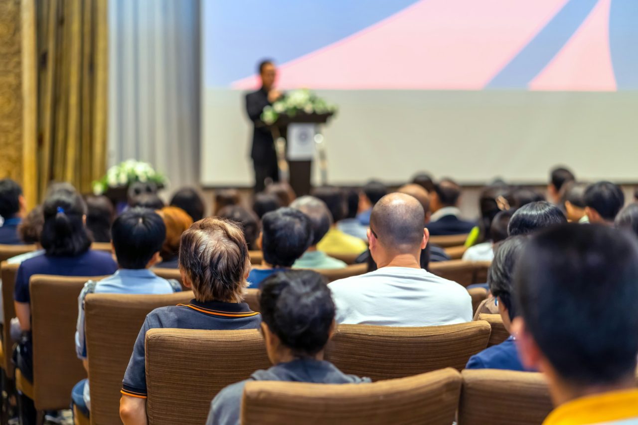 back-side-of-audience-listening-the-speaker-with-podium-on-the-stage-in-the-conference-hall.jpg